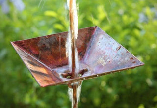 Shallow square cup rain chain with copper finish in use, water flowing outdoors.