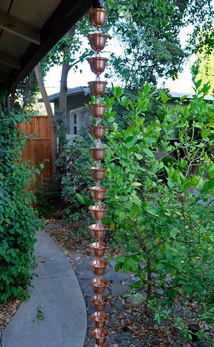 Full view of a copper spotted bell cup rain chain hanging in a garden.