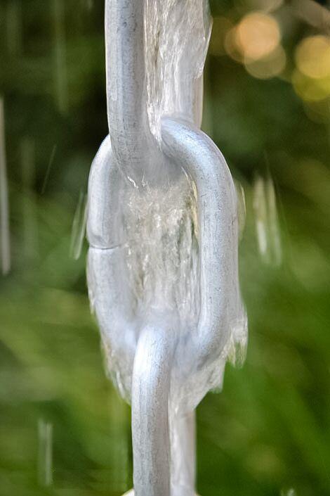 Detailed view of water flowing through a silver rain chain link.