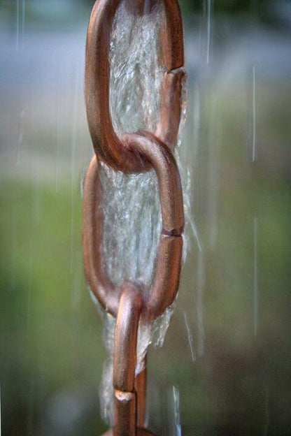 Close-up of water flowing through a copper-finished rain chain link.