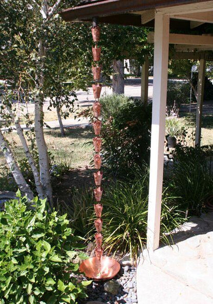 Full view of copper rain chain with sun face design, installed as a garden water feature.