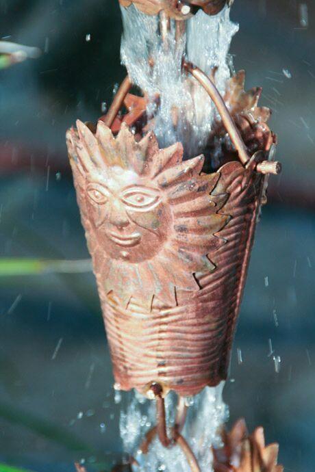 Close-up of copper rain chain featuring intricate sun face design with water cascading.