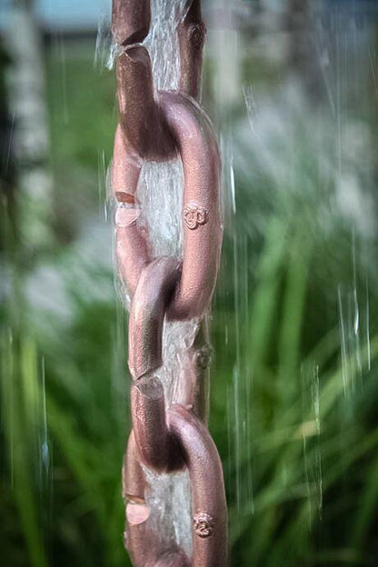 Copper rain chain with water flowing through thick cast links.