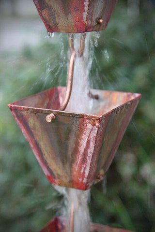 Water flowing through copper patina square cups of a rain chain in a garden.