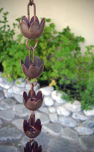 Full view of a tulip copper cup rain chain hanging outdoors with a garden backdrop.