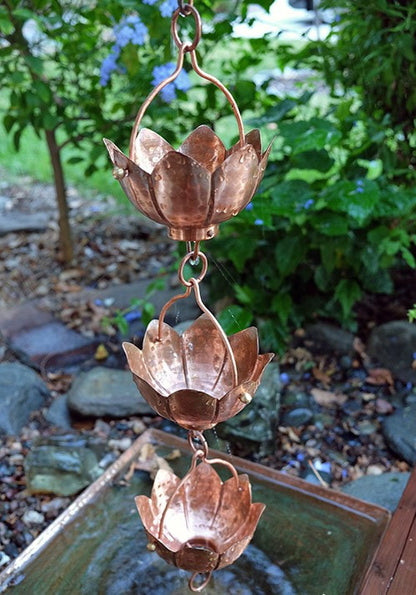 Copper lotus flower rain chain displayed in a garden setting.