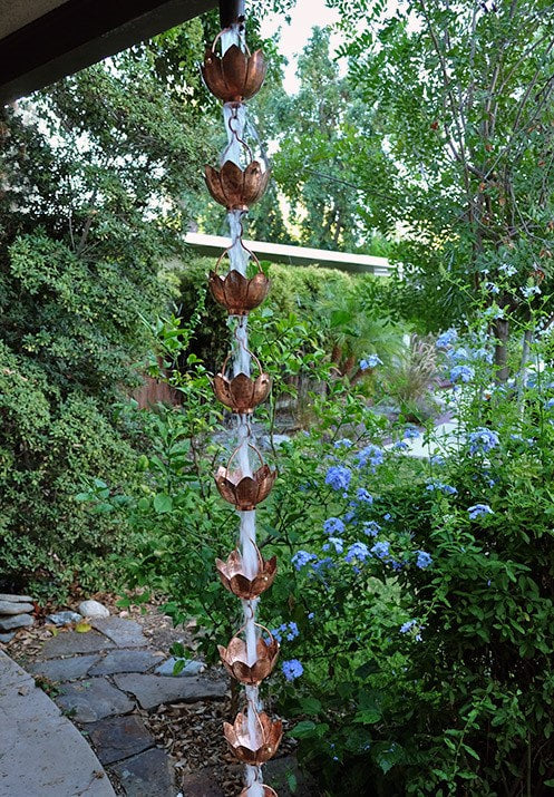 Full-length copper lotus flower rain chain hanging outdoors.