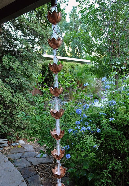 Full-length copper lotus flower rain chain hanging outdoors.