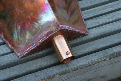 Detailed view of copper leaderhead outlet on wooden surface.