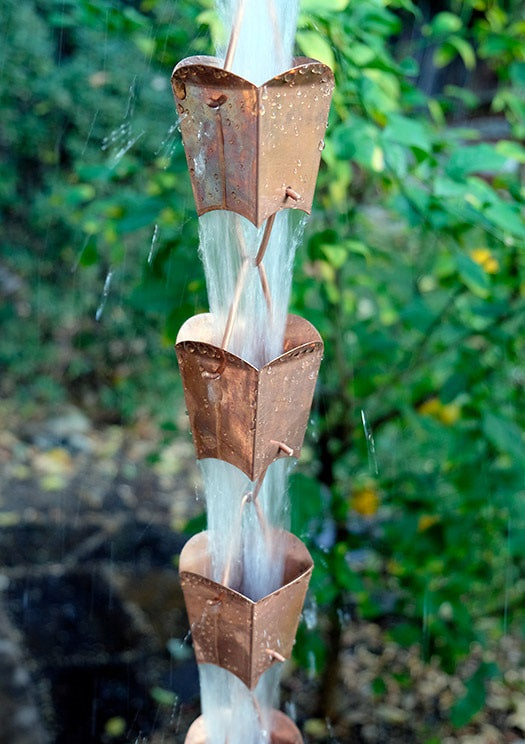 Multiple square tulip cups on a copper rain chain with water flowing down.