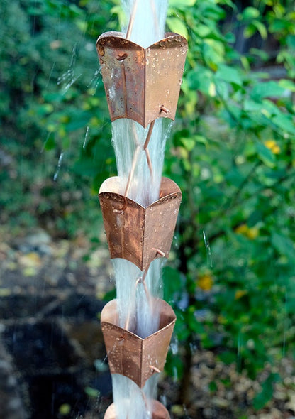 Multiple square tulip cups on a copper rain chain with water flowing down.