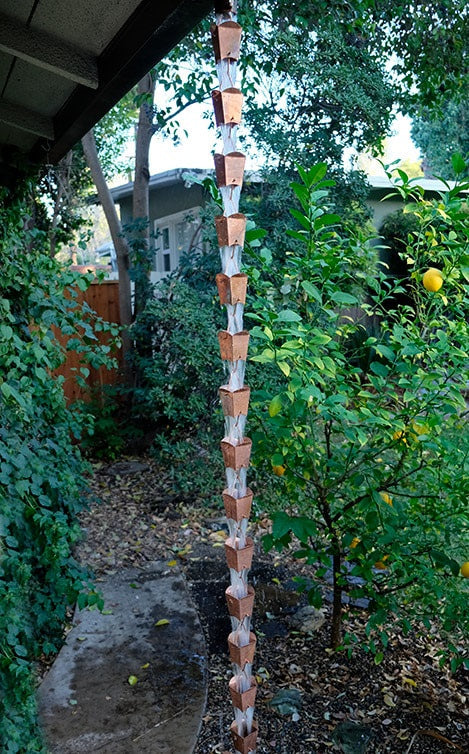 Full-length view of a copper square tulip cup rain chain installed in a garden.
