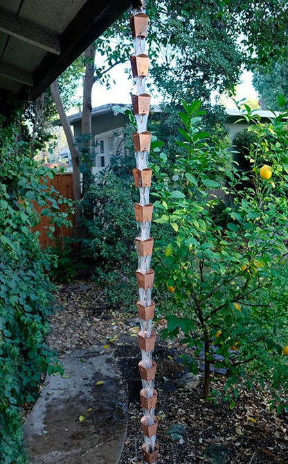 Full-length view of a copper square tulip cup rain chain installed in a garden.