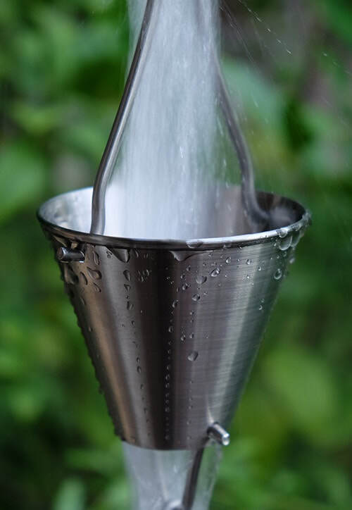 Close-up of stainless steel rain chain cup with water and droplets.